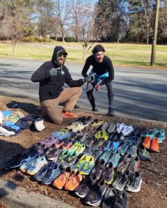 Two runners kneeling beside rows of old running shoes collected for GotSneakers